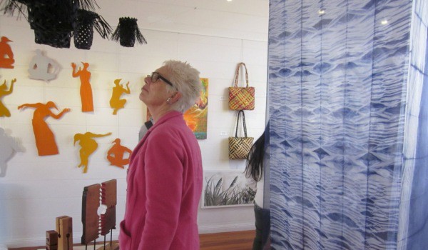 Silk artist Jean Carbon, flanked by her own work on the right, studies hanging raranga baskets by Ruth Port