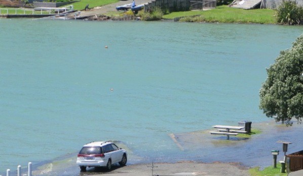Picnic table surrounded by a moat and water lapping around wheels of a parked car at end of Lorenzen Bay Road